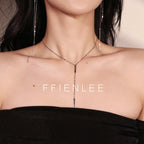 Half-body shot of model wearing FFIENLEE 925 sterling silver Y-lariat tile chain necklace with double bar pendant in 24K gold tone, paired with matching long tassel earrings, styled with a black off-shoulder dress, warm beige studio background, FFIENLEE branding