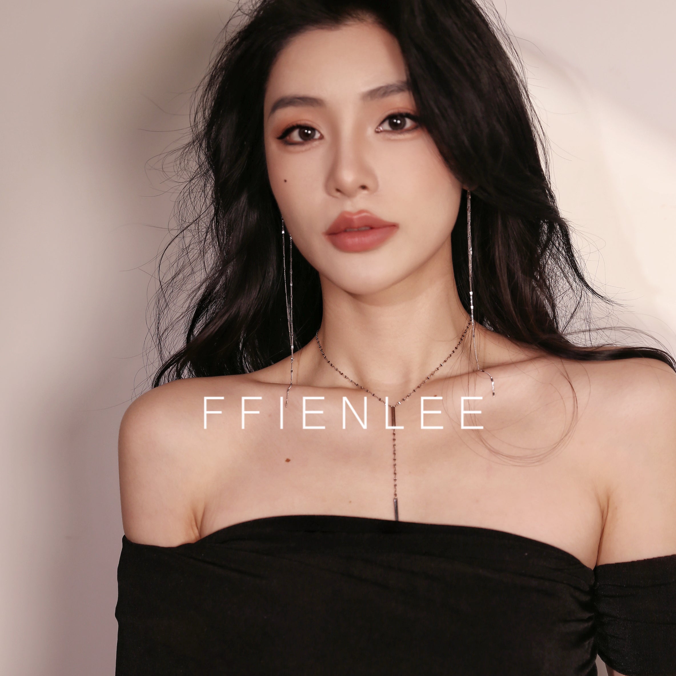 Close-up of model's neck and collarbone wearing FFIENLEE 925 sterling silver Y-lariat tile chain necklace with double bar pendant in 24K gold tone, paired with long tassel earrings, styled with a black strapless top, warm beige background