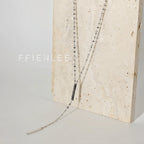 FFIENLEE 925 sterling silver Y-lariat tile chain necklace with double bar pendant in rhodium silver tone, draped against a textured cream travertine stone surface, showing full chain length, Y-drop, and both bar pendants, light grey background, FFIENLEE branding